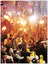色とりどりの祭り看板やのぼりが上がる中たくさんの松明の火が上がる「テ―ビー」の様子の写真