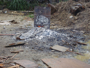 ドラム缶で出来た炉と大量の灰の写真